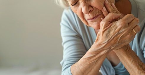 Eine Person verzieht vor Schmerz das Gesicht und hält sich die Schulter, was auf Schmerzen oder Unwohlsein hindeutet.