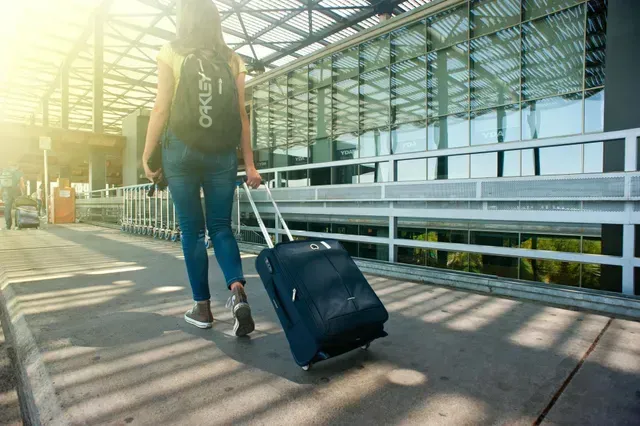 Mulher com mochila e uma mala de rodinhas andando numa passarela