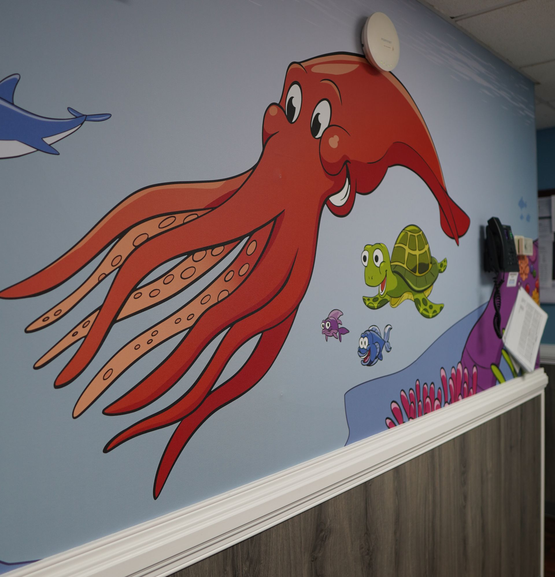 A mural on a blue wall featuring a large, smiling red octopus, a green turtle, a dolphin, and small fish.