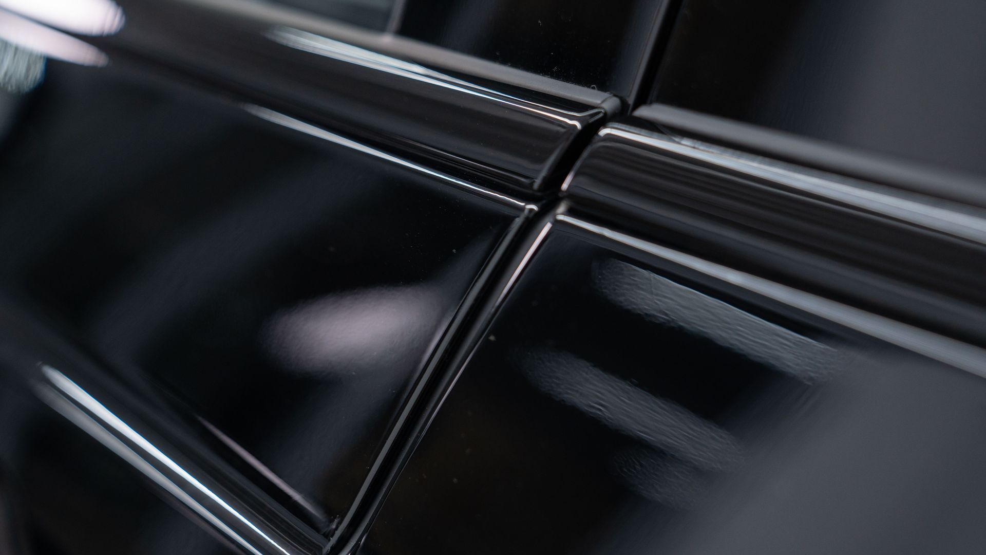 Close-up of glossy, dark-colored car paneling. Lines and curves reflect light, creating highlights.