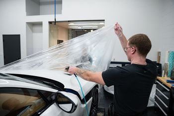 A man is wrapping a car with a plastic sheet.