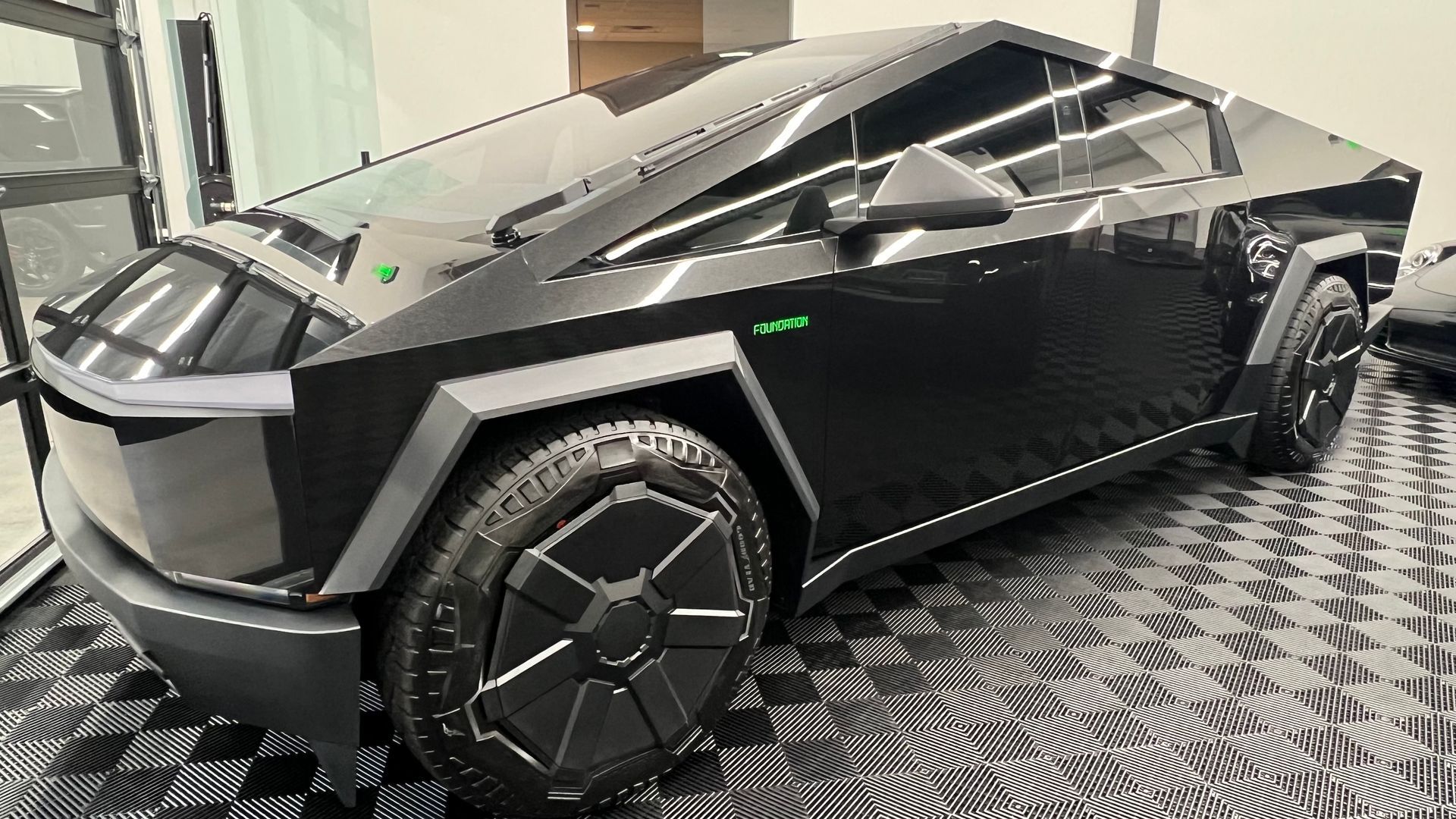 Black Tesla Cybertruck with angular design and unique black wheels, parked indoors.