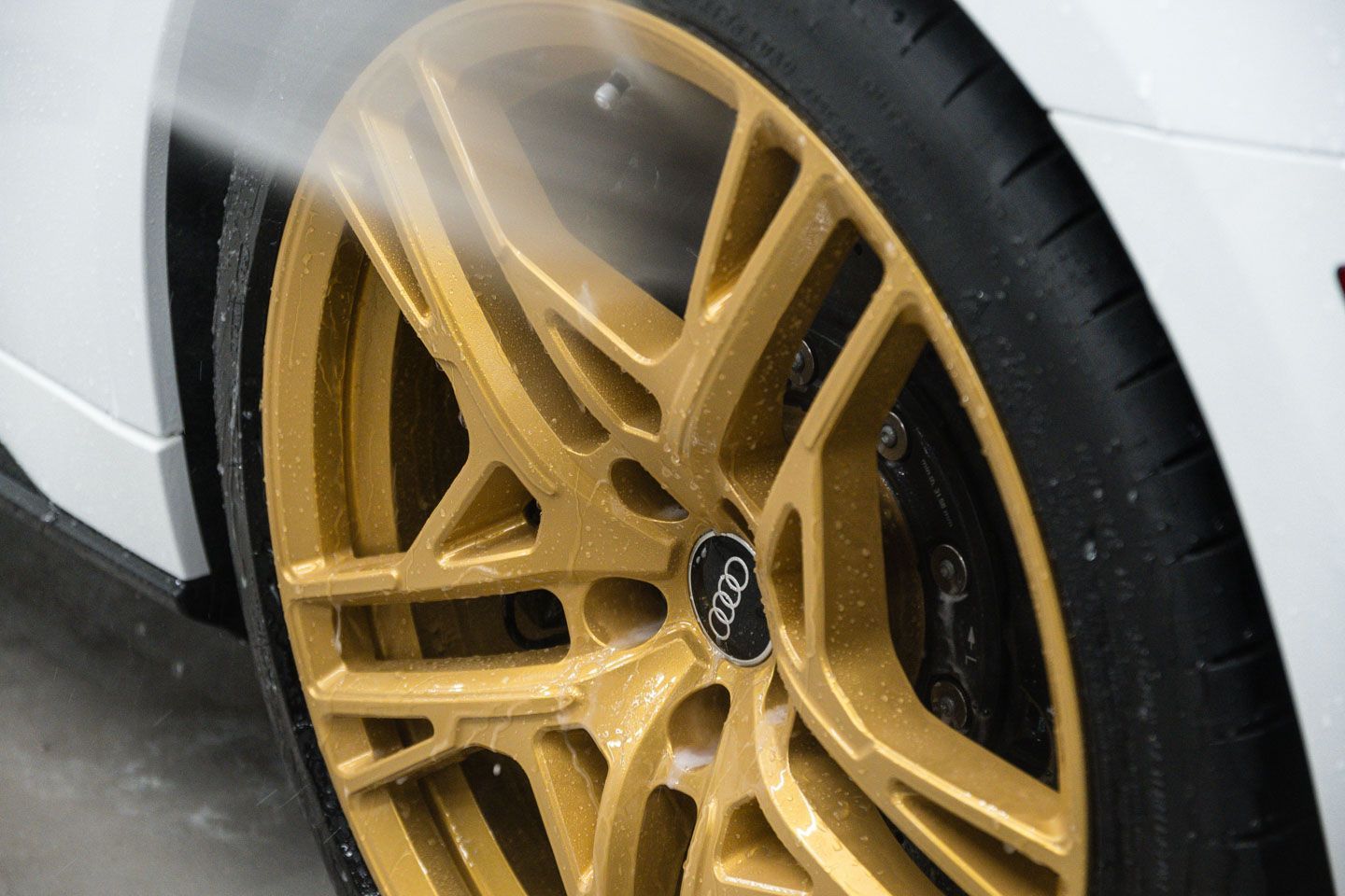 A person spraying water on a gold car wheel. The wheel is attached to a white car.