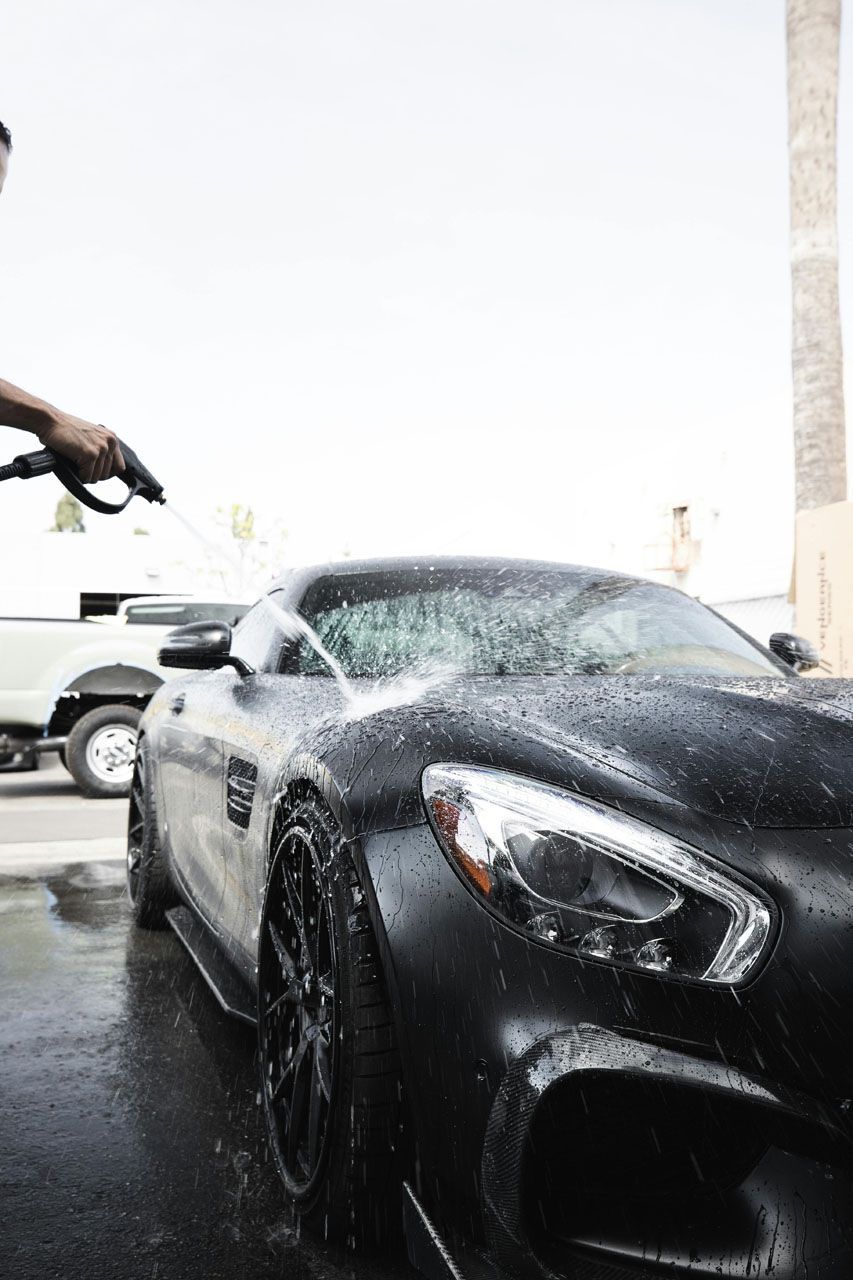 A person washes a matte black sports car with a hose.