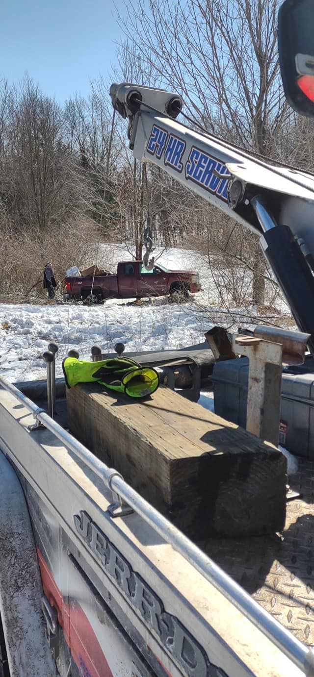 Yellow excavator lifting a concrete block from a snowy roadside worksite