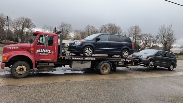 Tow truck hauling two SUVs on a flatbed along a wet roadside