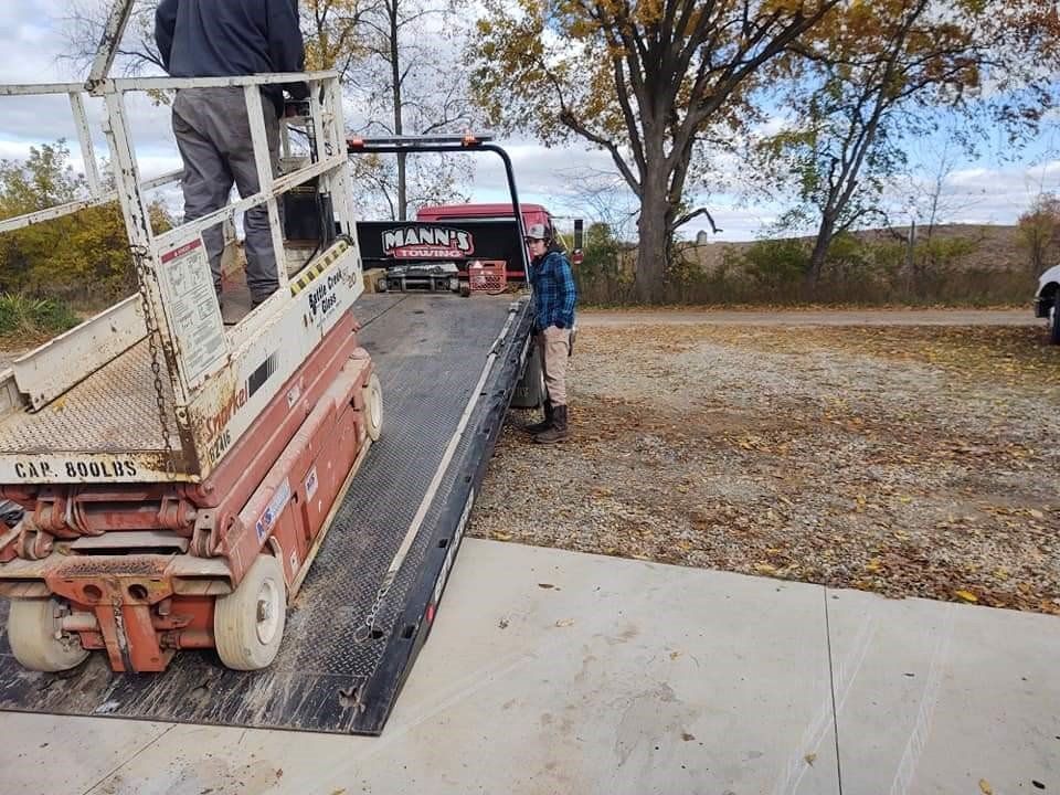Workers unloading a truck onto a driveway beside a leafless tree and open field