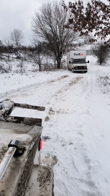 Snowy dirt road with a FedEx truck ahead and a vehicle hood in the foreground