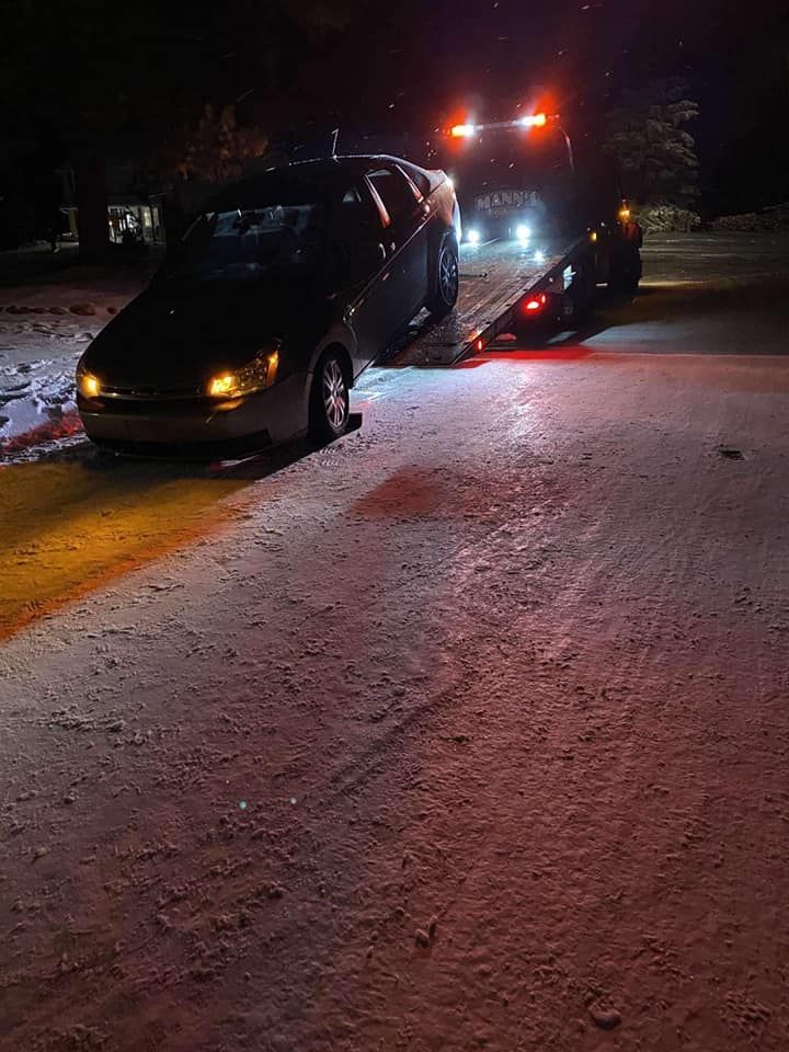 Tow truck loading a black van on a snowy road at night, with flashing amber lights