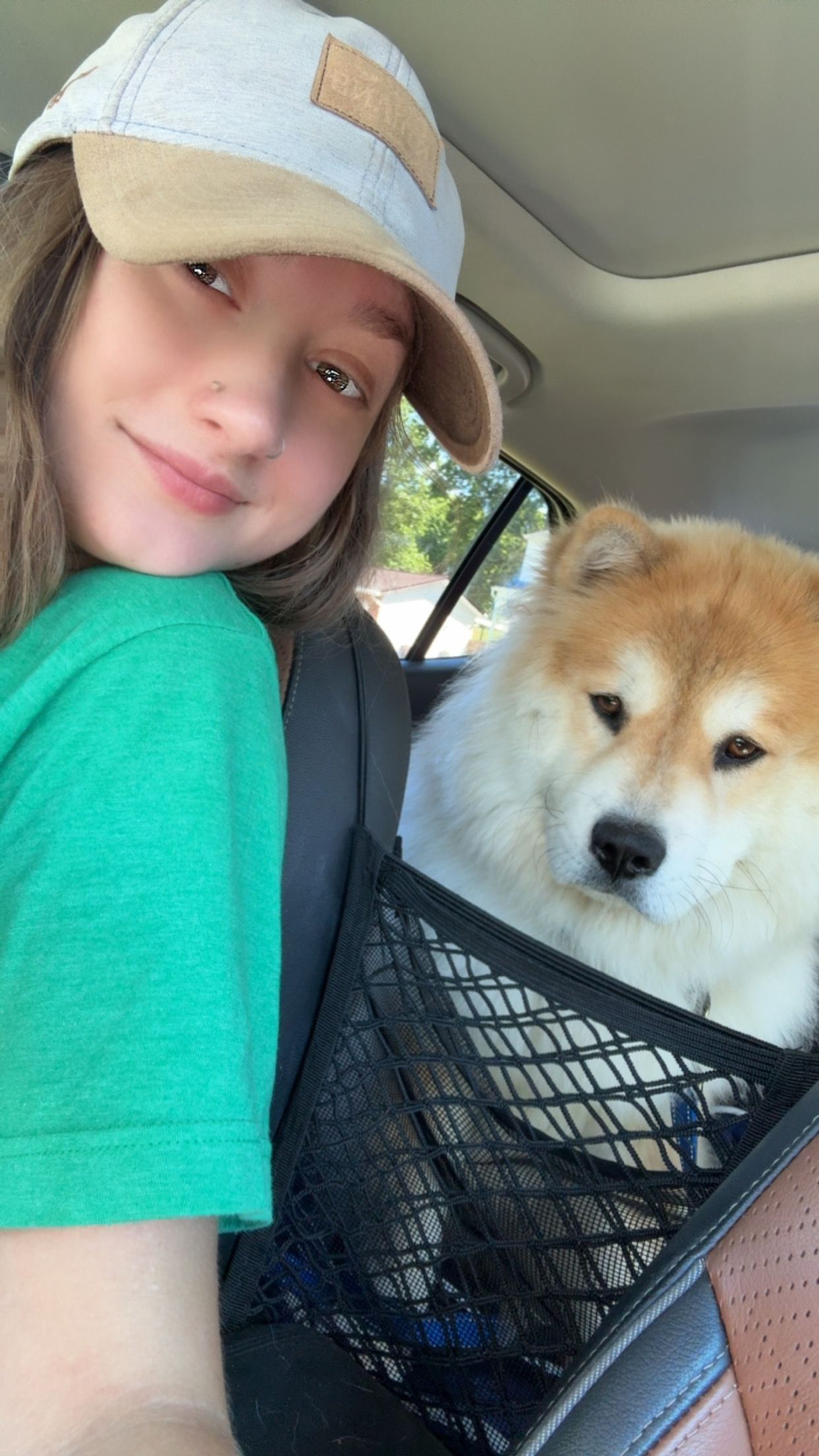 Lex in green shirt and hat smiles with a Chusky dog in a car's cargo net.