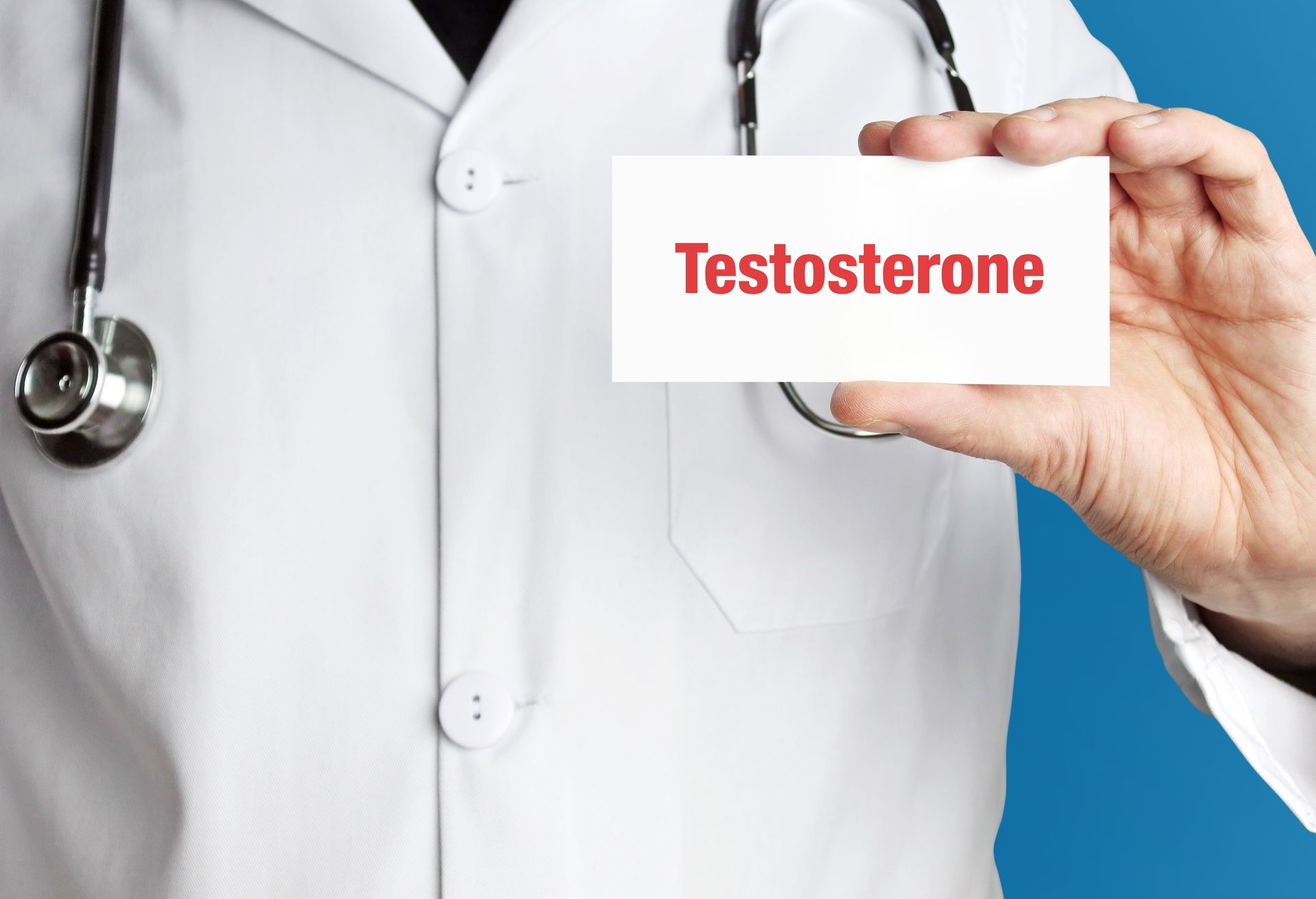 A doctor in blue gloves holding a testosterone card with a stethoscope and notepad.