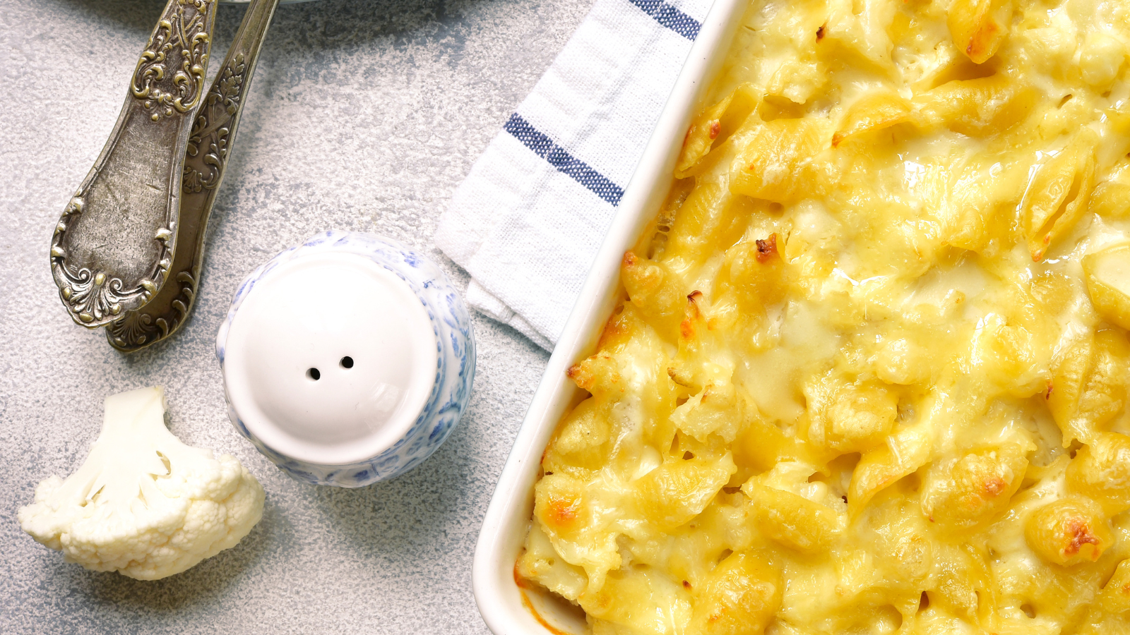 Macaroni and cheese casserole in white dish, with cauliflower and salt shaker.