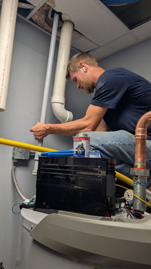 Technician repairing a pipe overhead in a utility room, with tools and equipment nearby.