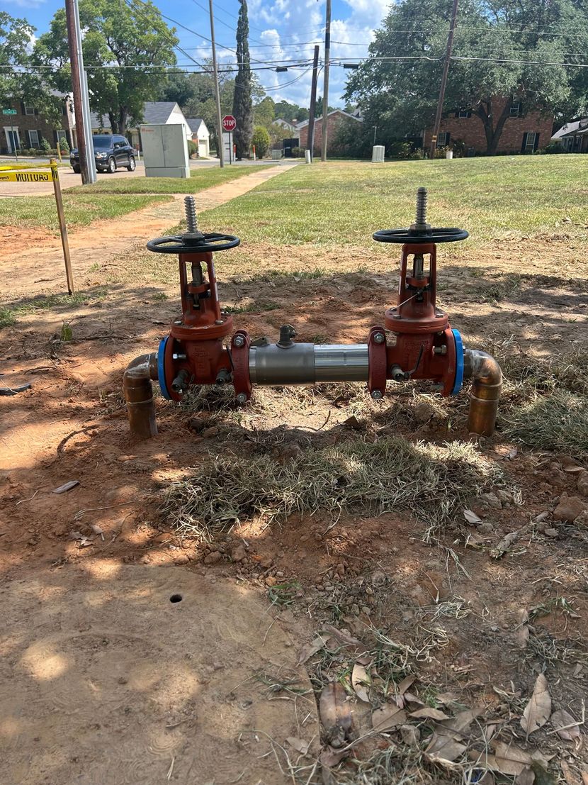 Two red fire hydrants connected by a gray pipe in a grassy park area
