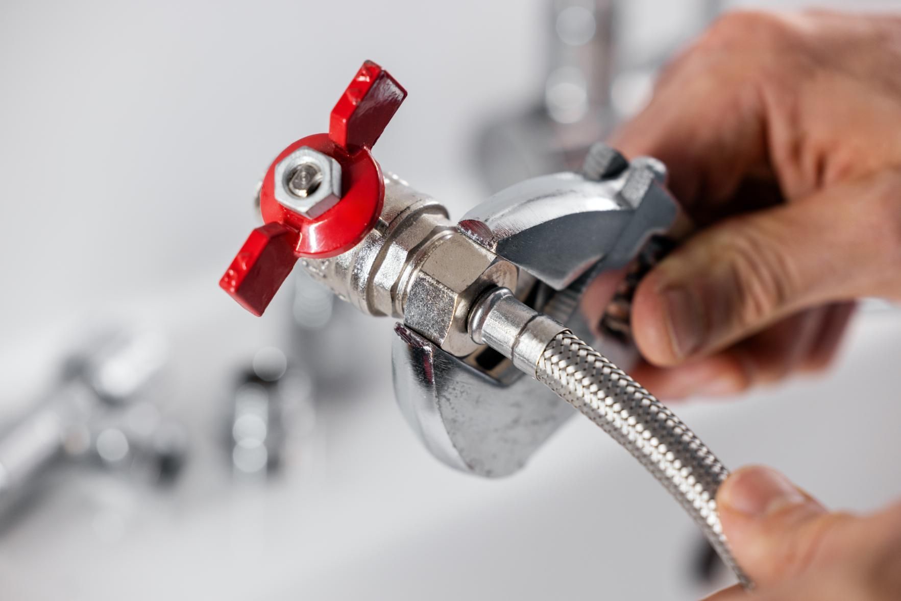 Hand connecting a braided hose to a chrome faucet valve with a red handle