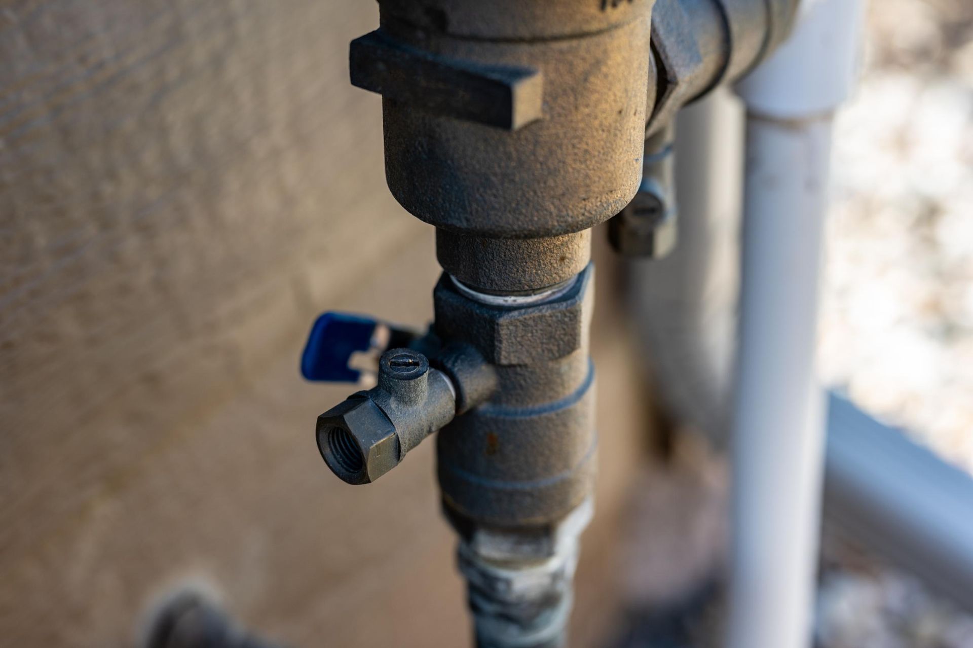 Close-up of a rusty outdoor pipe valve with a blue handle against a wall