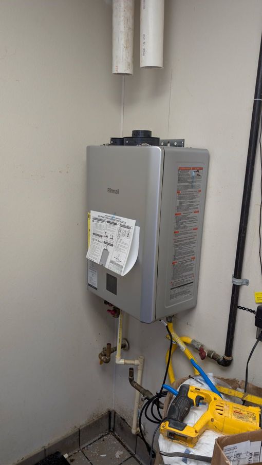 Gray wall-mounted water heater with pipes and attached labels in a utility room