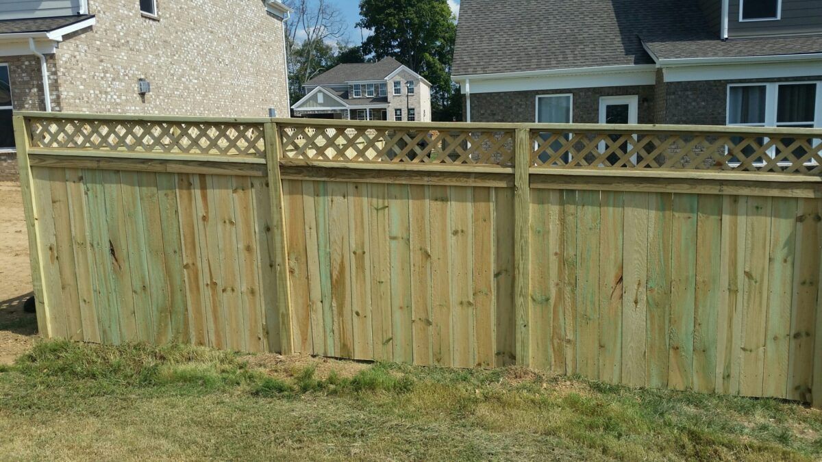 A new wooden privacy fence with a lattice top section, set in a residential yard with houses in the background.