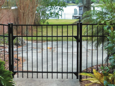 A black metal gate stands as a barrier on a paved walkway, overlooking a grassy lawn and a body of water.