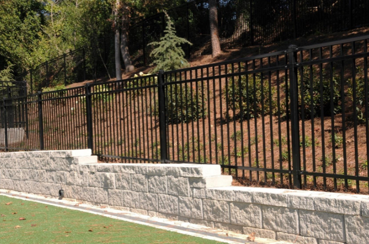 A new wooden scalloped-top privacy fence installed on a residential lawn with houses in the background.
