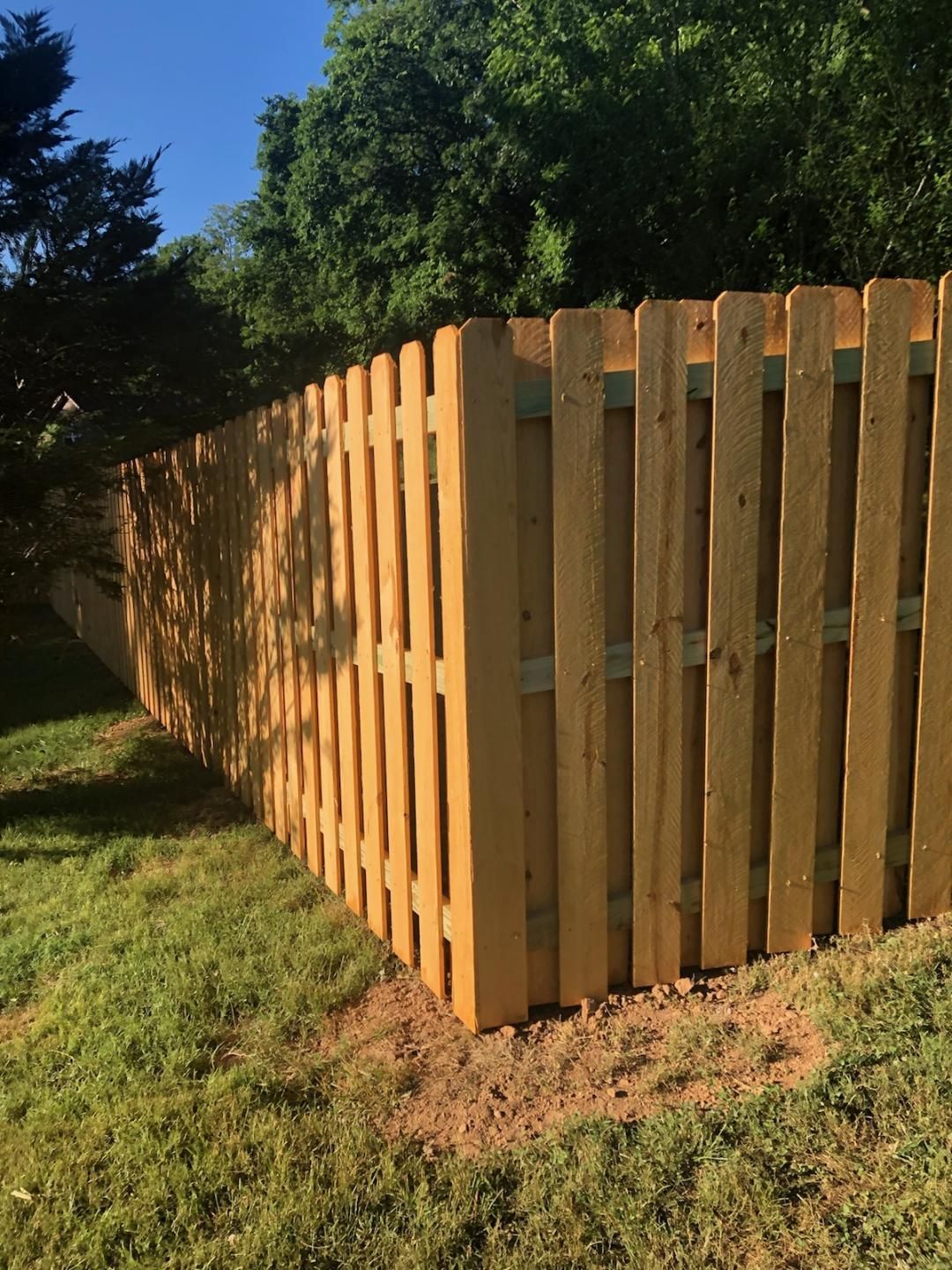 A new wooden privacy fence in a sunny backyard, viewed at a corner where two sections meet over grass.