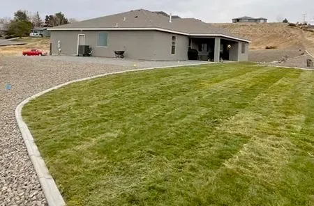 Gravel driveway beside a green lawn leading to a gray house with an attached covered patio.