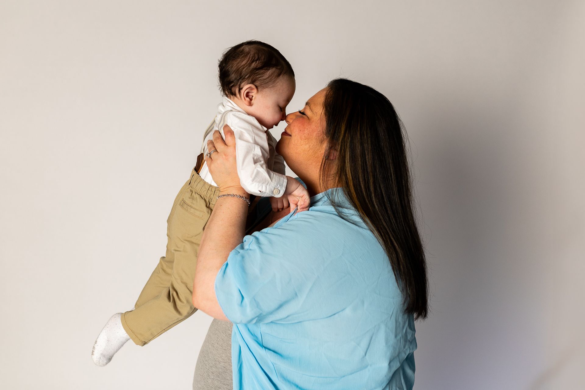 Adult in blue shirt holding and kissing a baby against a plain wall - family photos