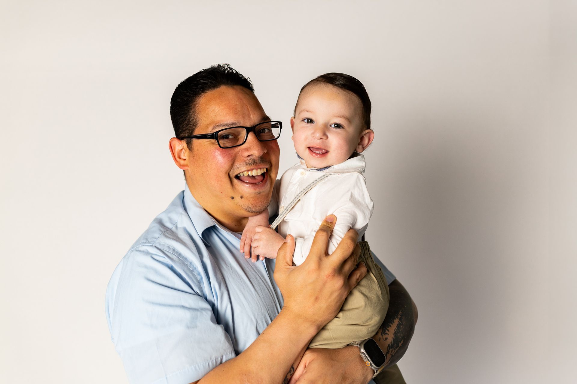 Smiling man holding a laughing baby against a plain light background - family photos