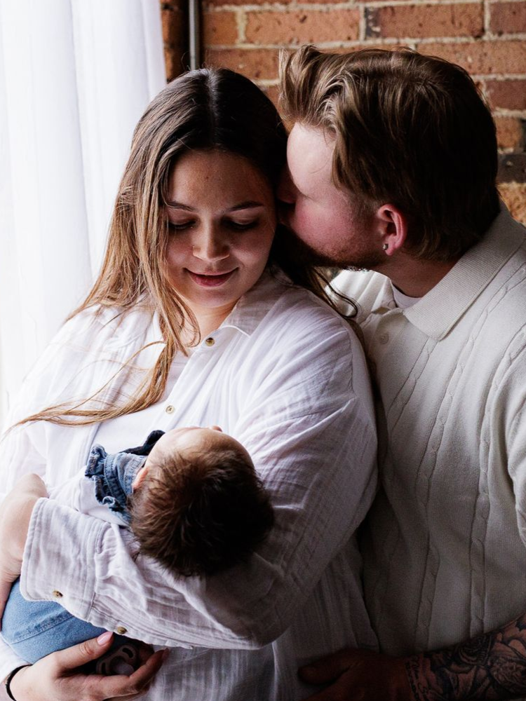 A man is holding a newborn baby wrapped in a green blanket.