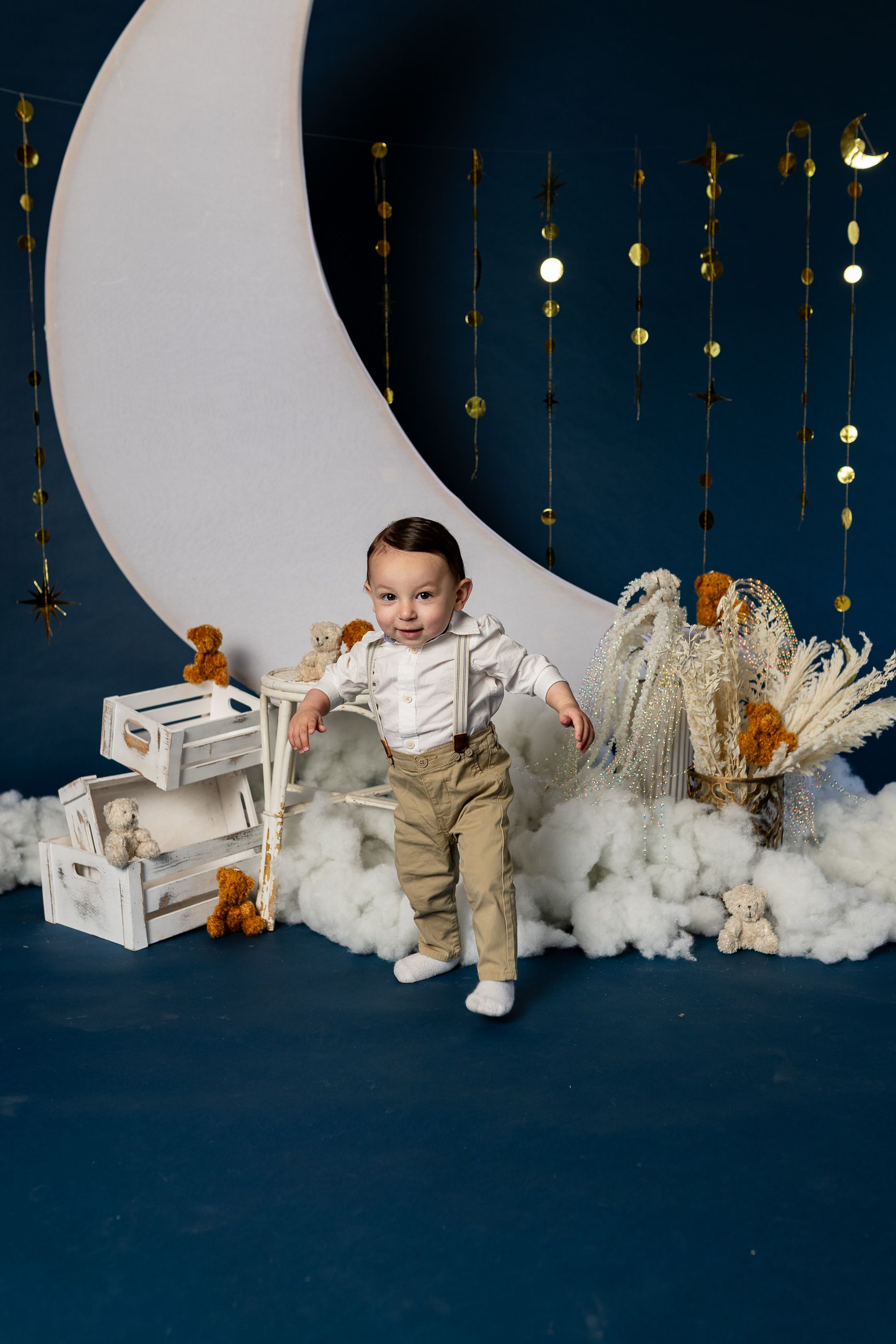 baby standing in a moon-themed studio set with clouds, stars, and teddy bears for cake smash session