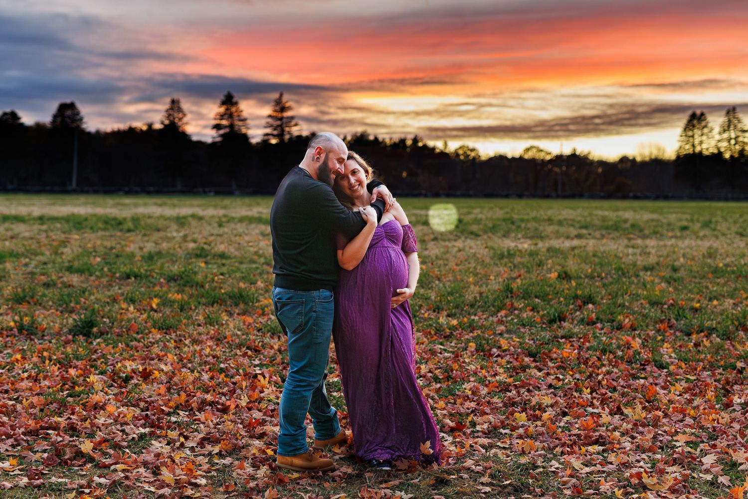 Maternity photography parents posing while snuggling together during sunset
