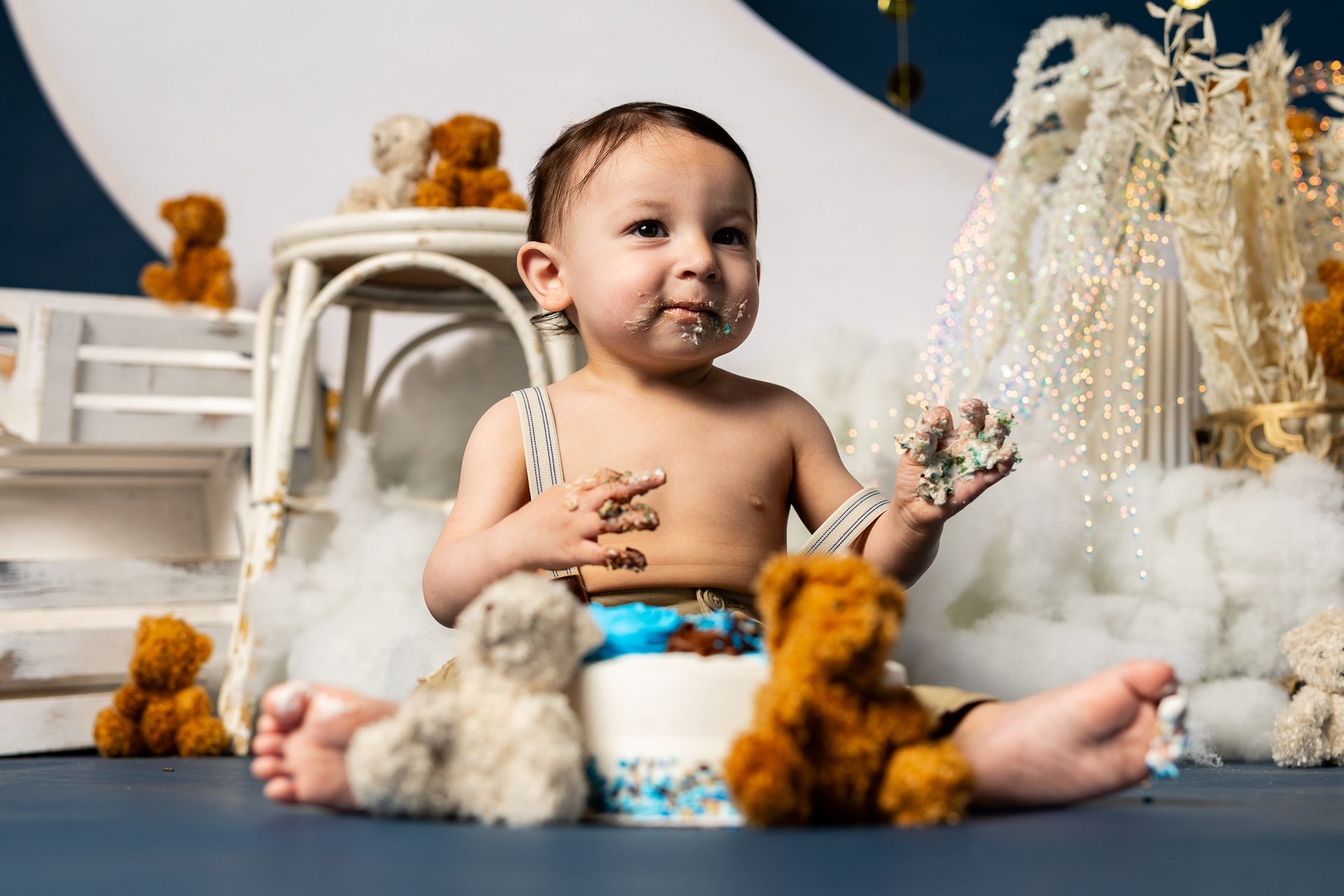 baby standing in a moon-themed studio set with clouds, stars, and teddy bears for cake smash session