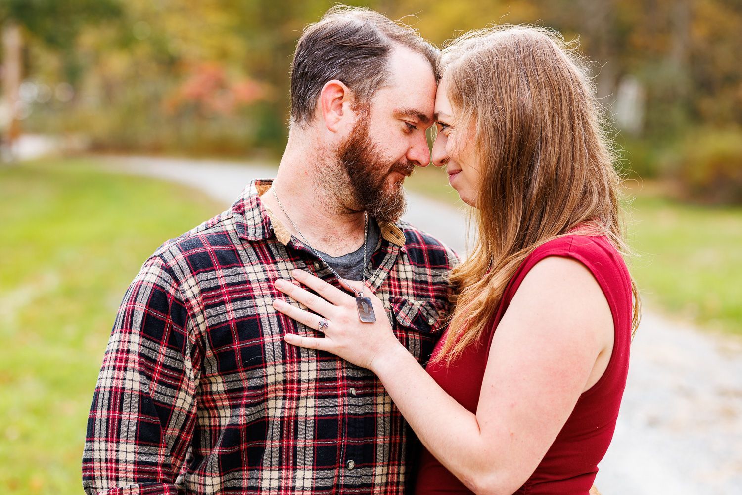 Couple touching foreheads in a park, smiling and embracing, with autumn trees in the background. - family photos