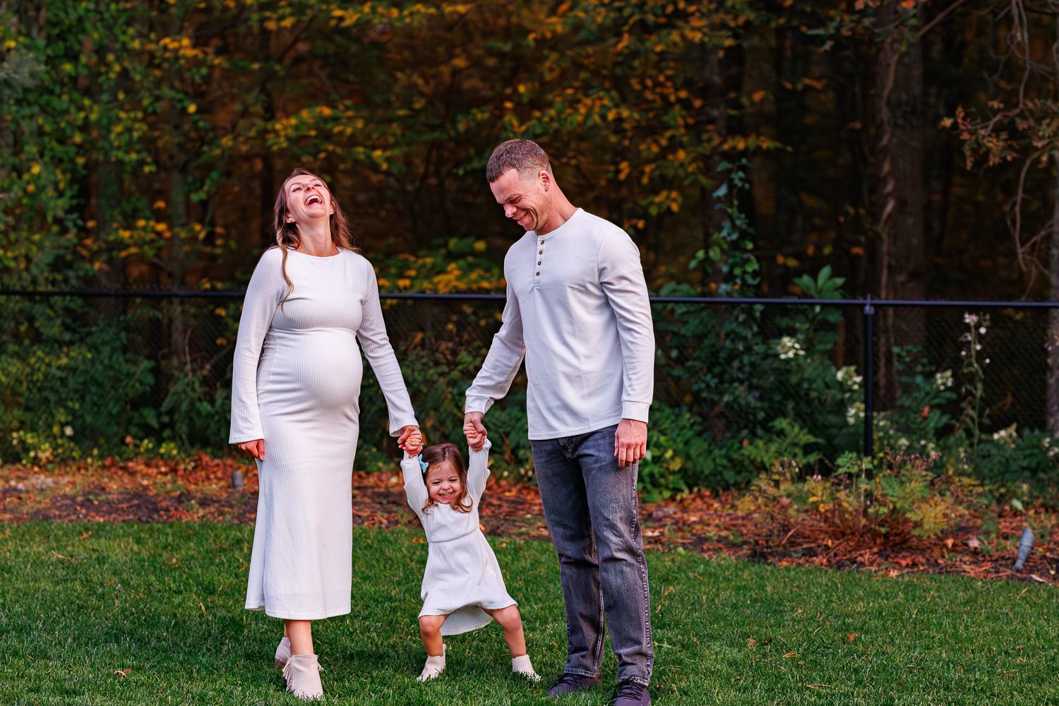 Maternity photography parents swinging toddler by hands and laughing