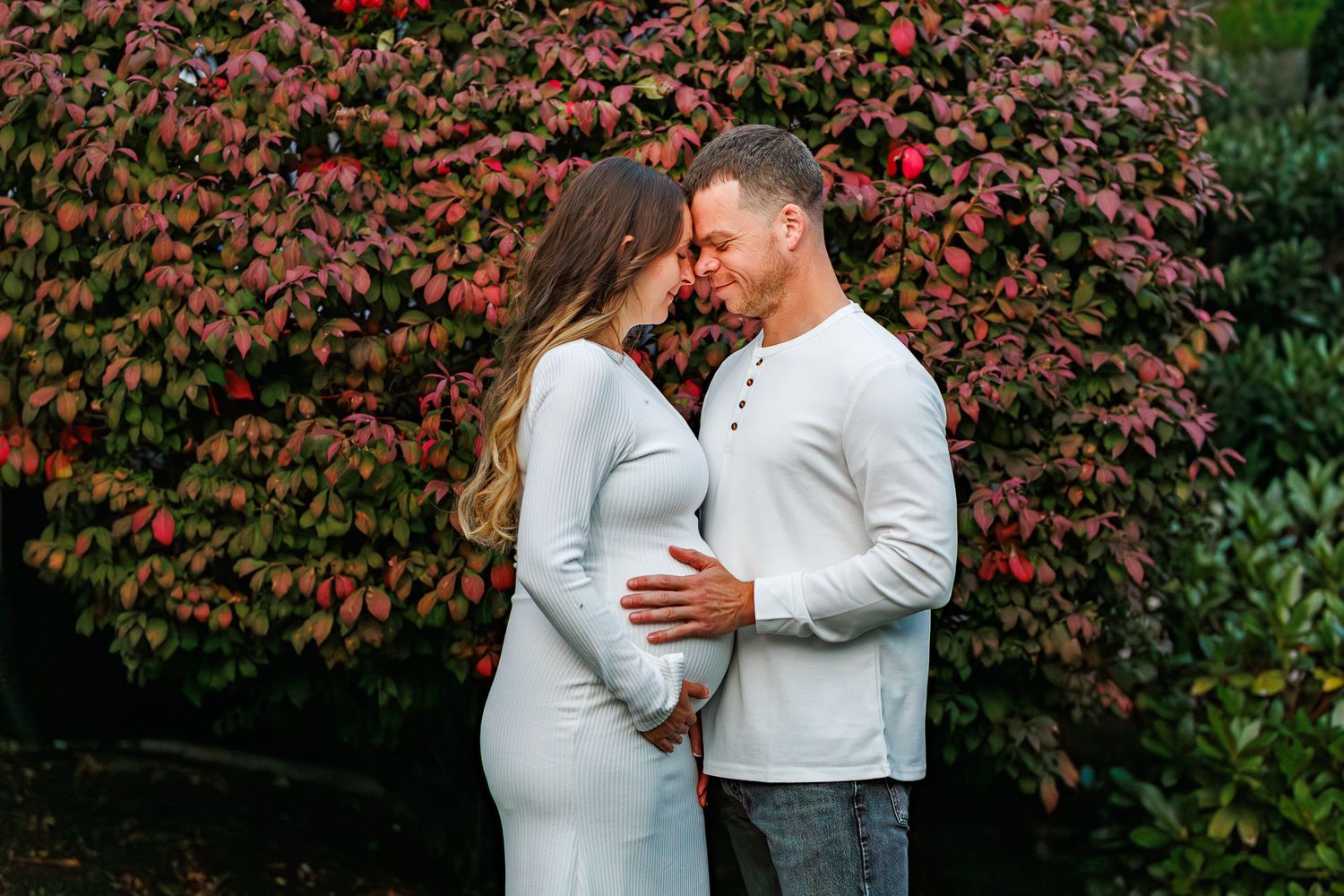 Maternity photography parents snuggled together in front of fire bush