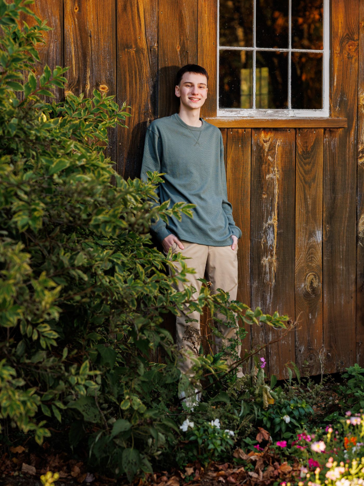 Photography MA -A young man is sitting on a wooden bench in front of a wooden building.
