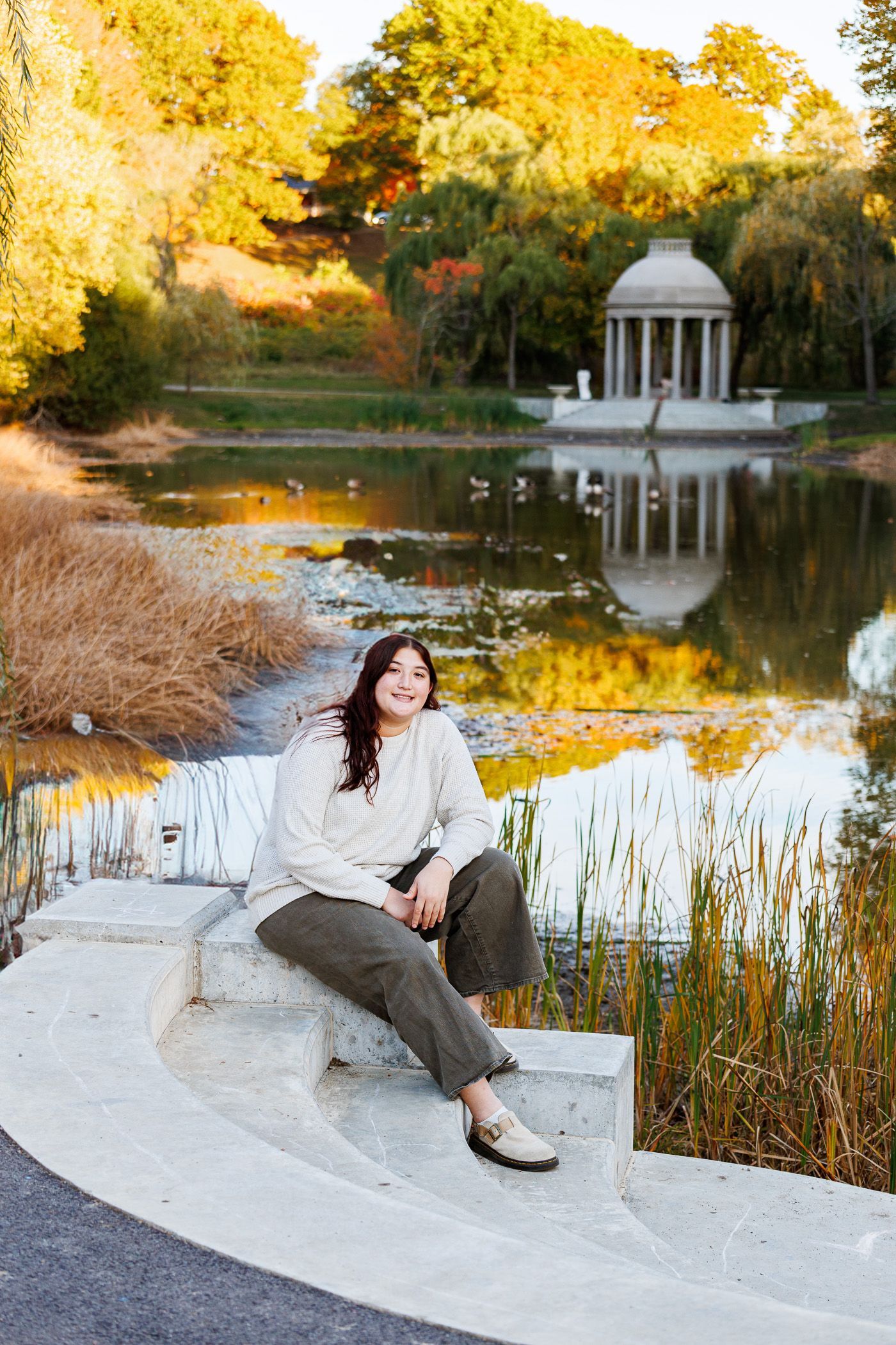 High school senior - senior photography - female student sitting by waterfront with stone gazebo in background