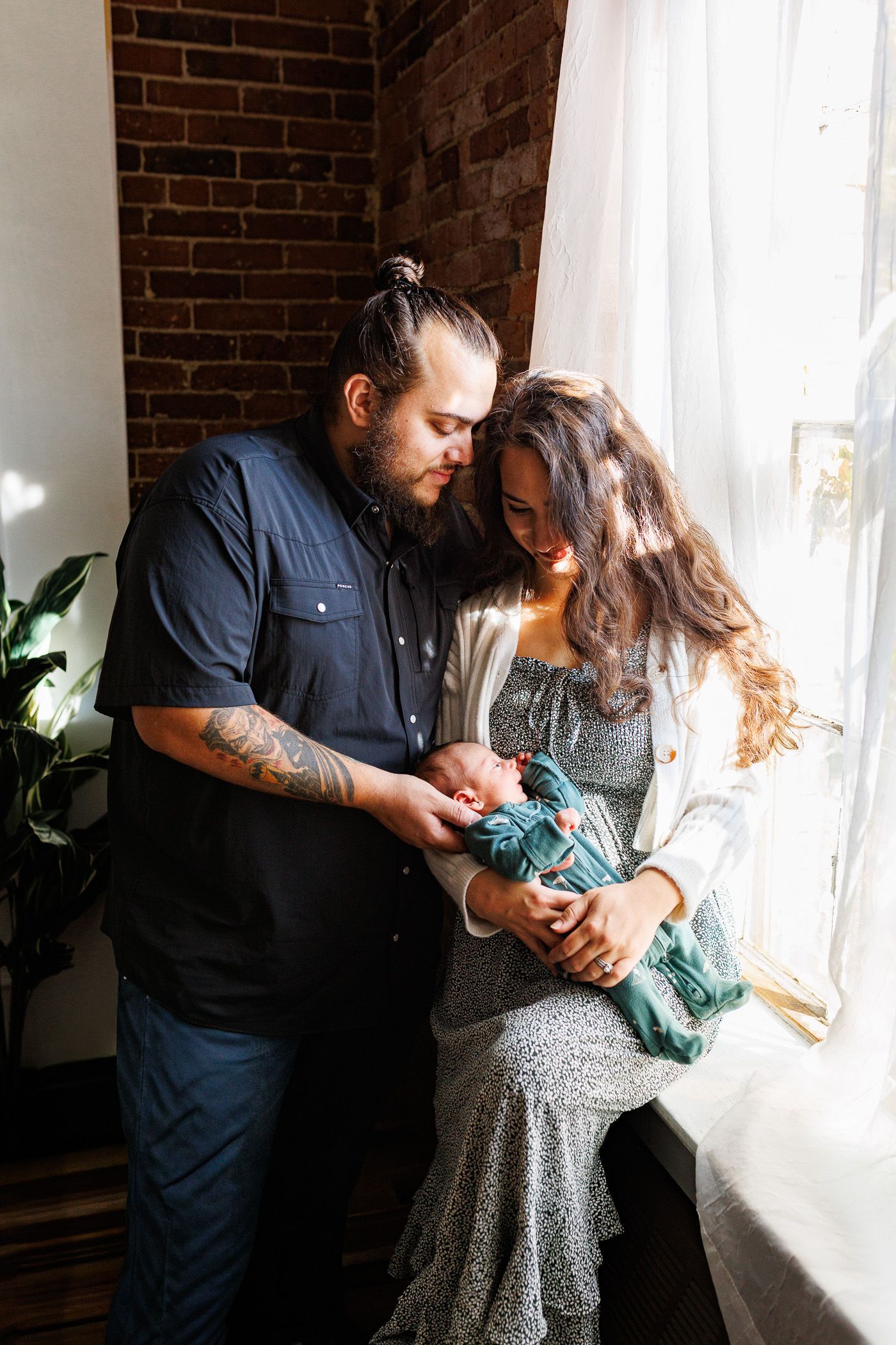Newborn photography parents standing by window with newborn
