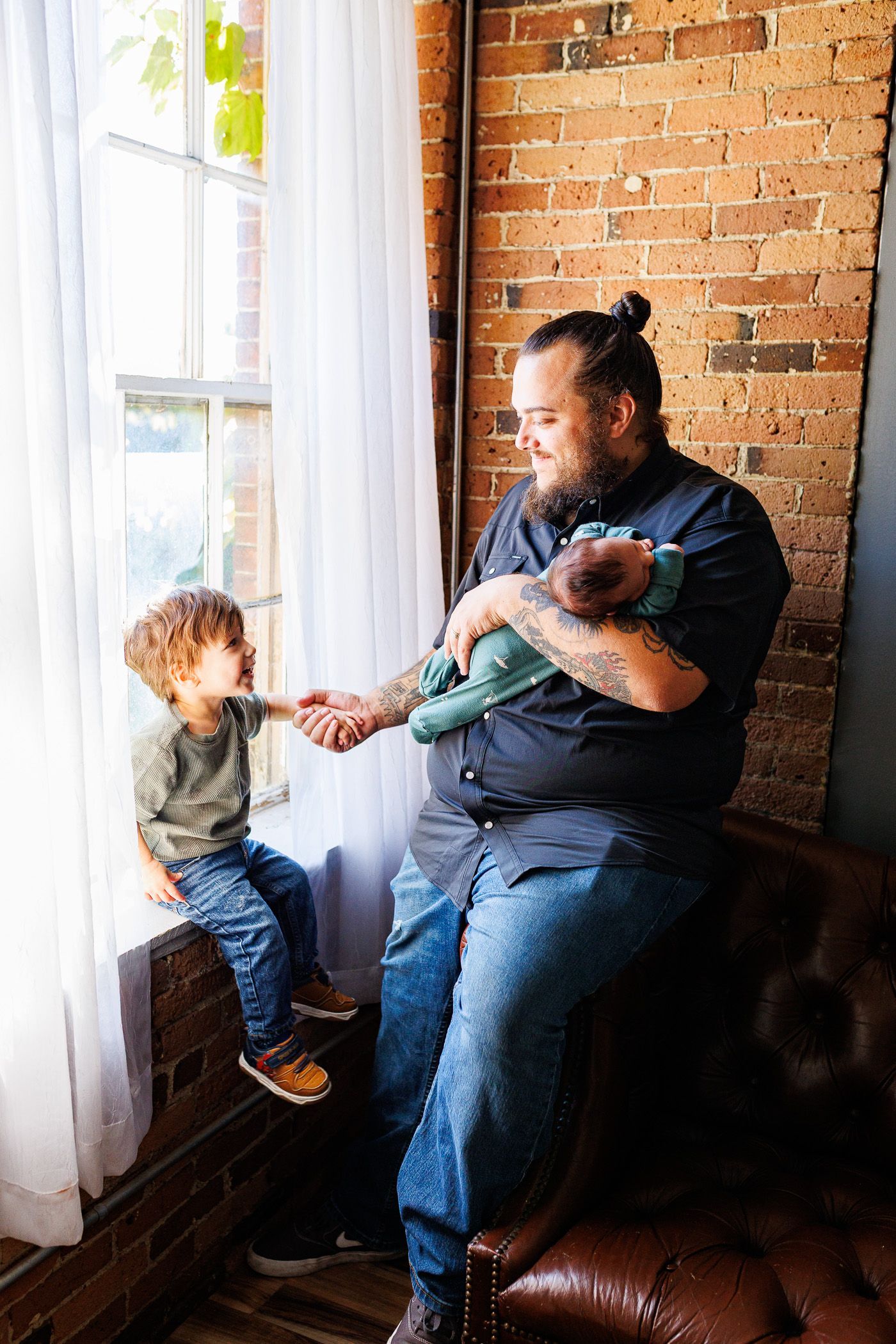 Newborn photography father standing by window with toddler and newborn