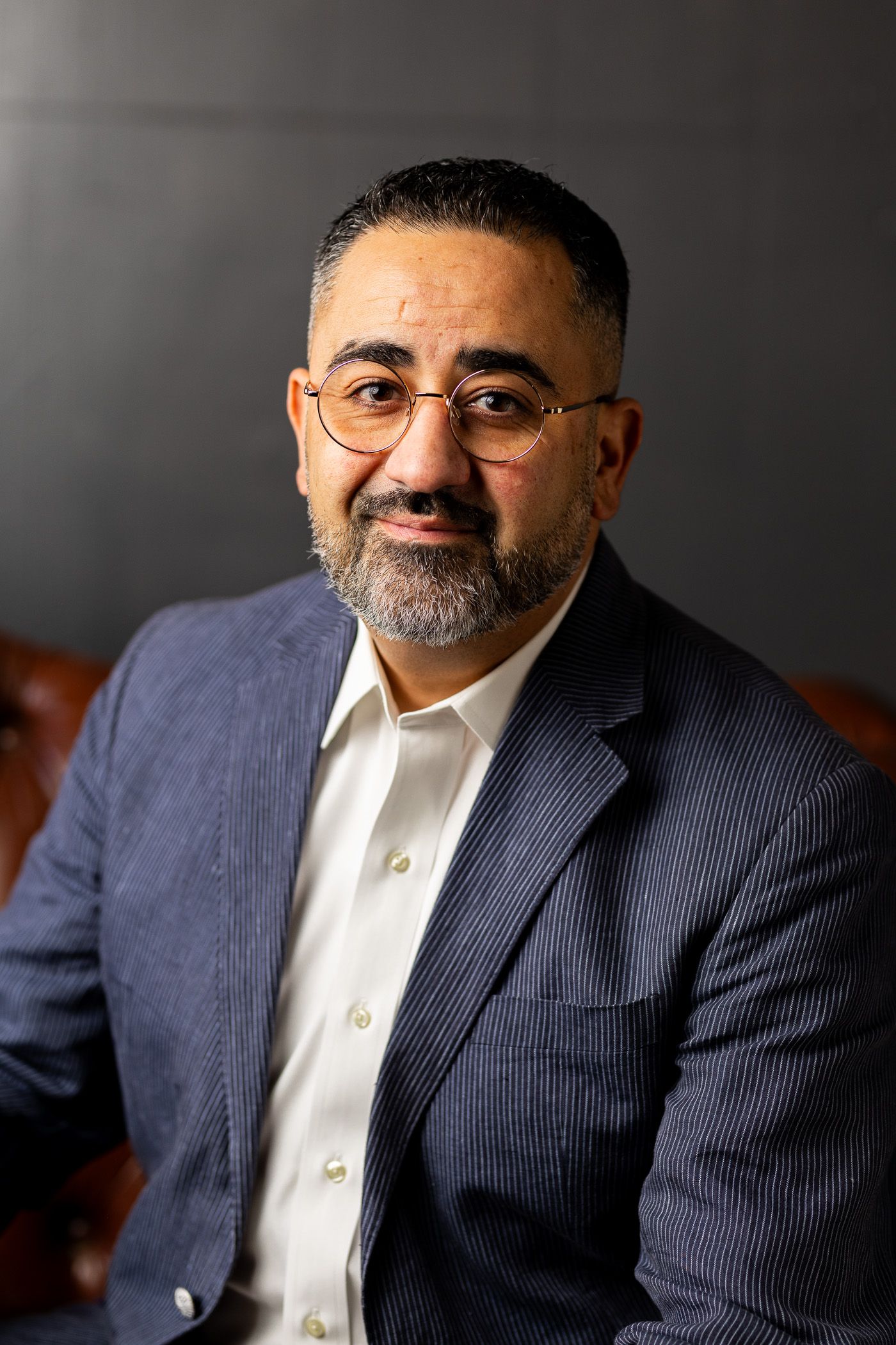 Man in a navy blazer and glasses smiling against a dark background - headshot session