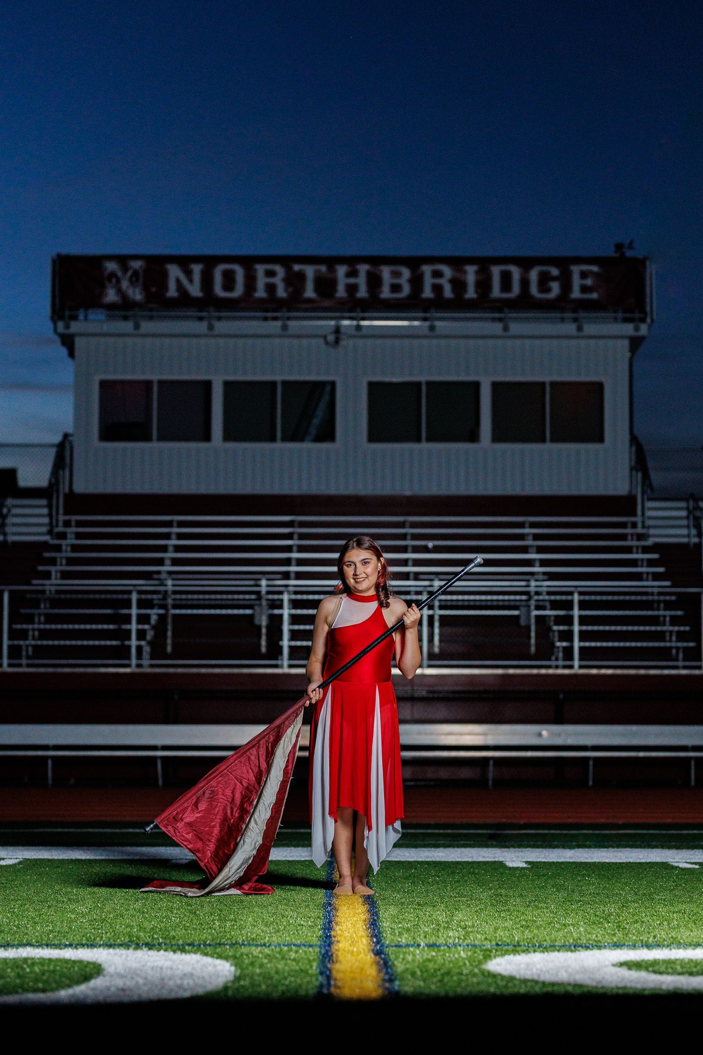 High school senior - senior photography - female student posing with color guard flag on football field