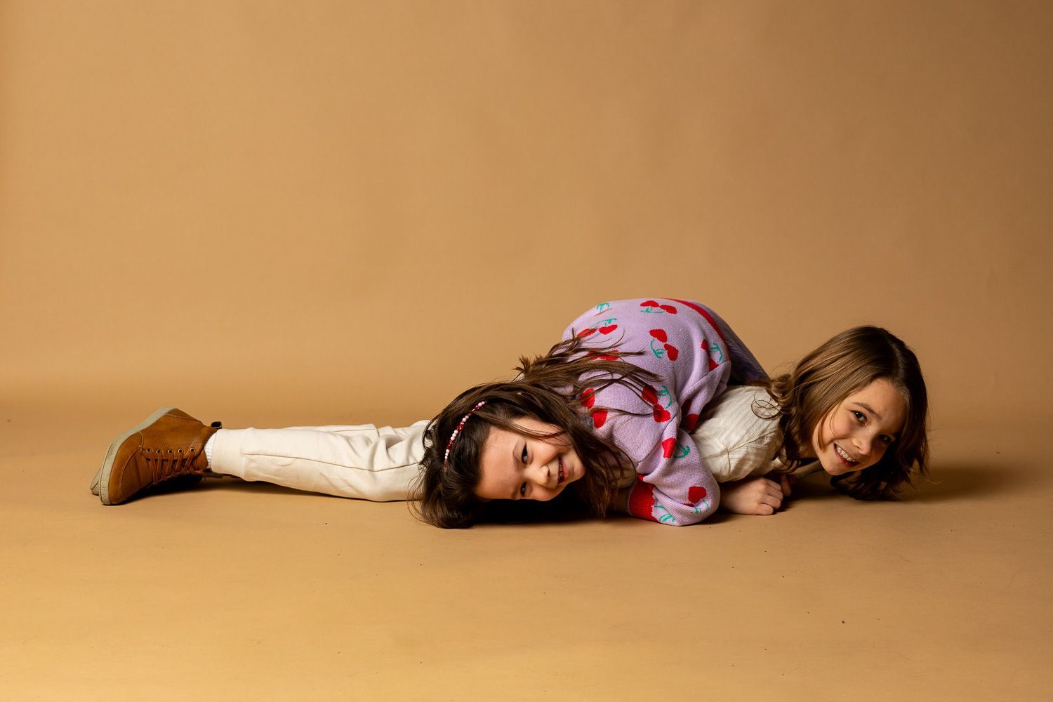 Two people lying on a tan floor against a tan backdrop, wearing patterned clothes and brown boots. - family photos