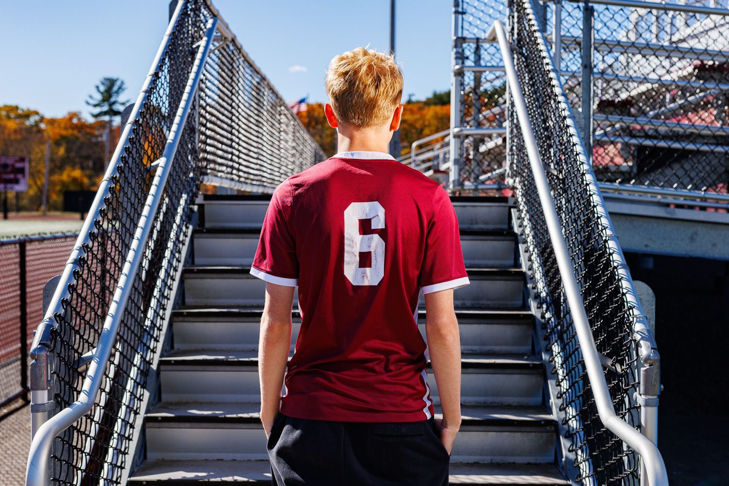High school senior - senior photography - male student posing by bleachers with soccer jersey