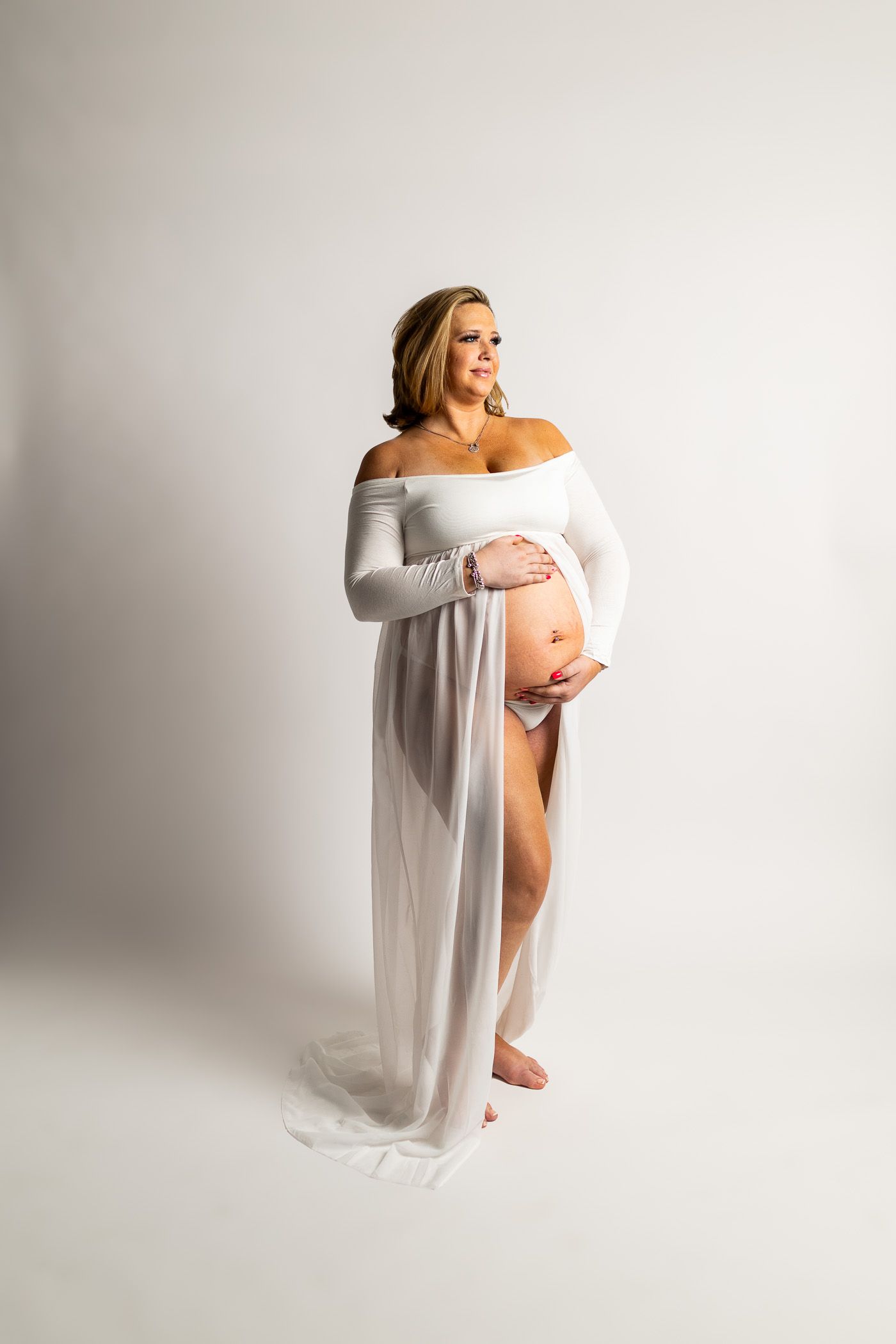 Maternity photography mom posing in white dress on white studio background