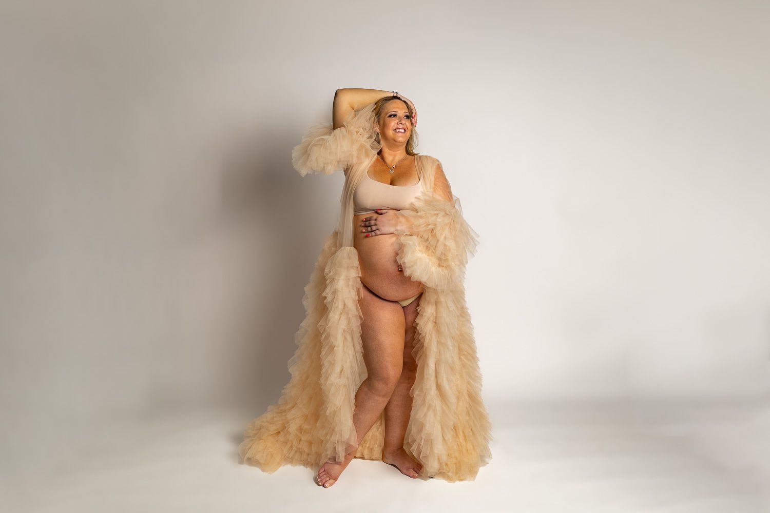 Maternity photography mom posing in tan robe on white studio background