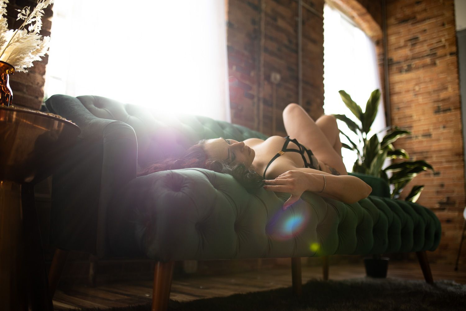 Woman posing in lingerie for boudoir session lying on a couch with a sun flare
