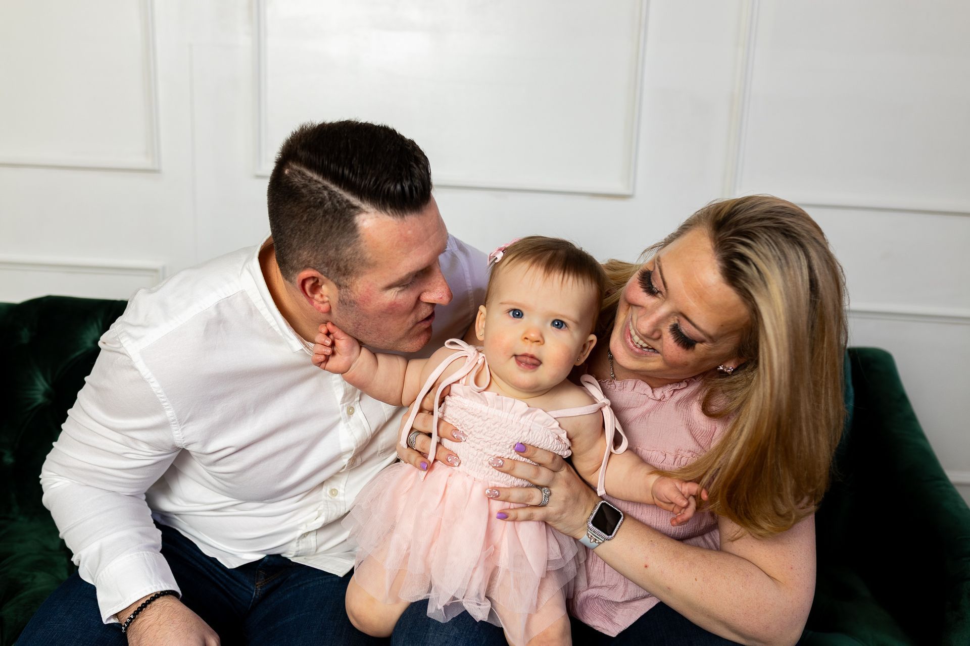 Family sitting on a couch, smiling at a baby in a pink dress - family photos