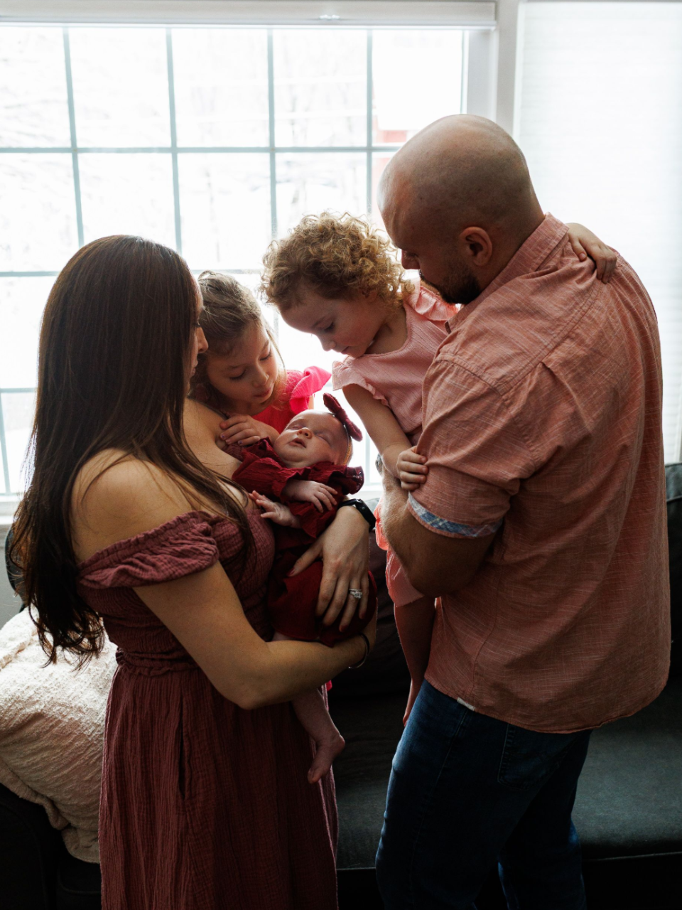 A man and woman are holding a newborn baby while a little girls looks on.