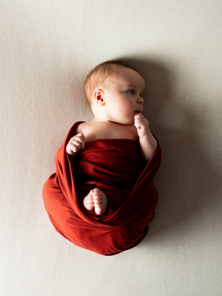A newborn baby is wrapped in a white blanket and wearing a pearl headband.