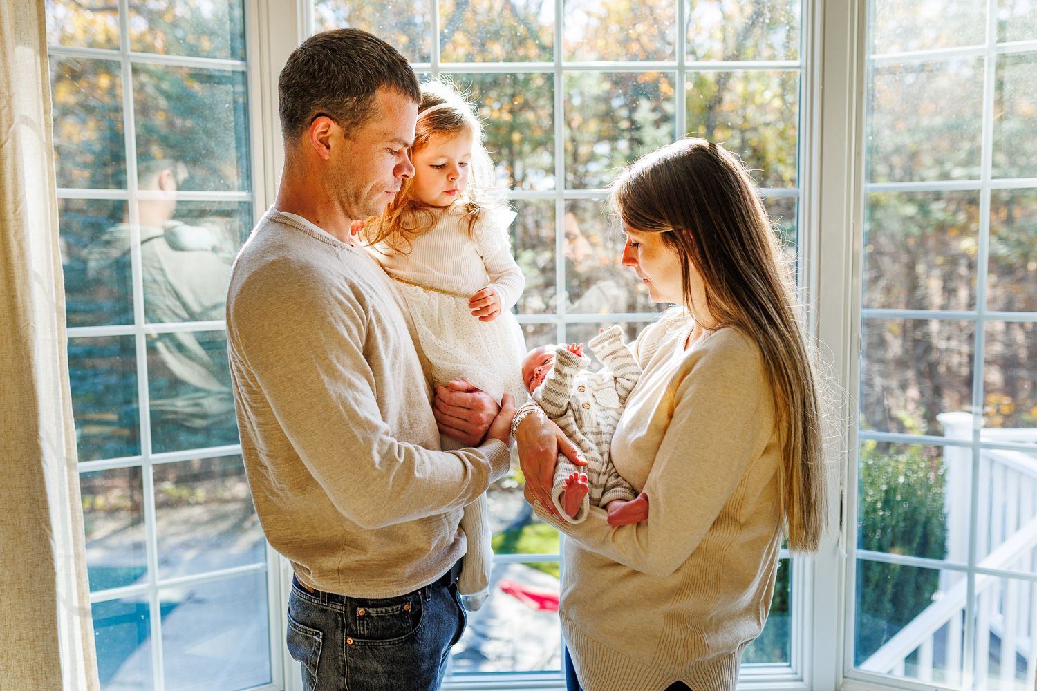 Newborn photography family posing by window with newborn baby